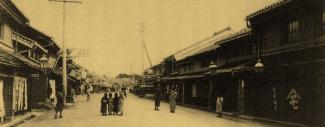 Image historique sepia d'une rue au Japon bordée de bâtiments en bois et en brique avec des toits de tuiles.