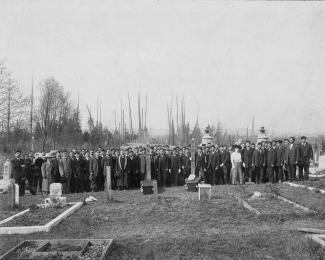 Sepia photo of large group of funeral attendees at gravesites. Trees visible behind them.