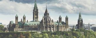 Image of Canada's Parliament buildings with greenery in front and cloudy grey sky.