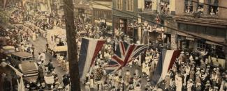 Image en couleur de canadiennes-japonaises paradant en kimono sur la rue Powell avec drapeau anglais en premier plan.