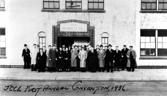 Black & white group photo of Japanese Canadians outside large building with '1928 Japanese Hall' inscribed above entryway.