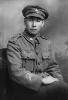 Black & white portrait of First World War Japanese Canadian soldier in uniform. His jacket and cap have maple leaf emblems.