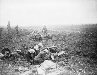 Image en noir et blanc de mitrailleurs canadiens couchés dans des trous d’obus avec des soldats debout au loin du paysage nu.