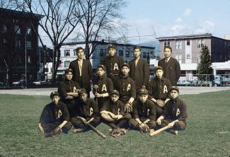 Sepia photo of male Japanese Canadian baseball team. Four men in back, four kneeling in middle, five sitting in front.