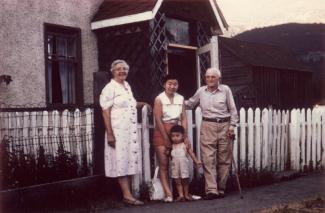 Japanese Canadian woman and child stand in front of a home and picket fence with an elderly man and woman.