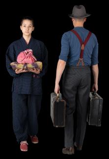 Colour photo of two youth in historical clothing on black background. One youth with his back turned holding two suitcases. 