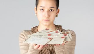 Image en couleur d'une jeune Canadienne Japonaise tenant dans ses mains plusieurs lettres historiques.