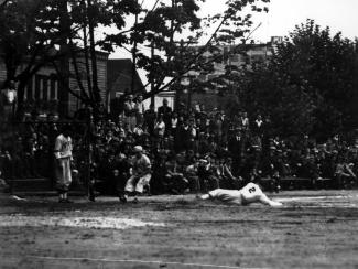 Black & white photo of a large crowd watching a baseball player sliding into home base.