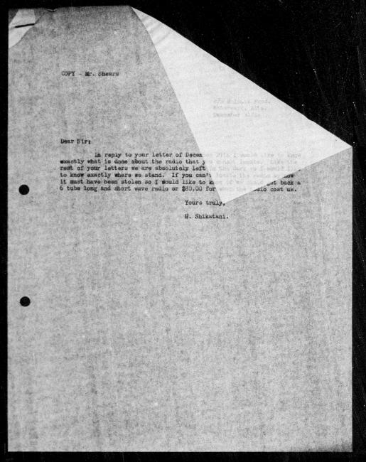 Un microfilm noir et blanc scanné d'une copie dactylographiée d'une lettre adressée au gouvernement de Hisajiro Shikatani concernant la dépossession de sa propriété. L'image a un coin replié qui obscurcit une grande partie de la lettre. On peut lire une partie à travers le pli, mais pas tout.
